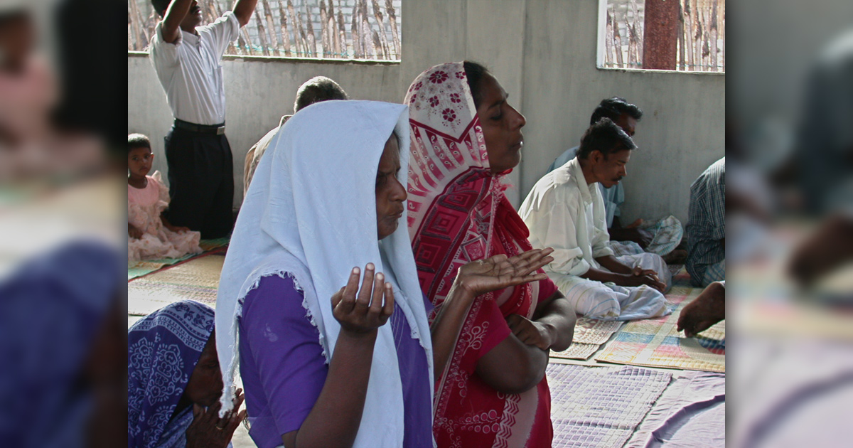 Two women praying in the foreground; others behind them, also praying