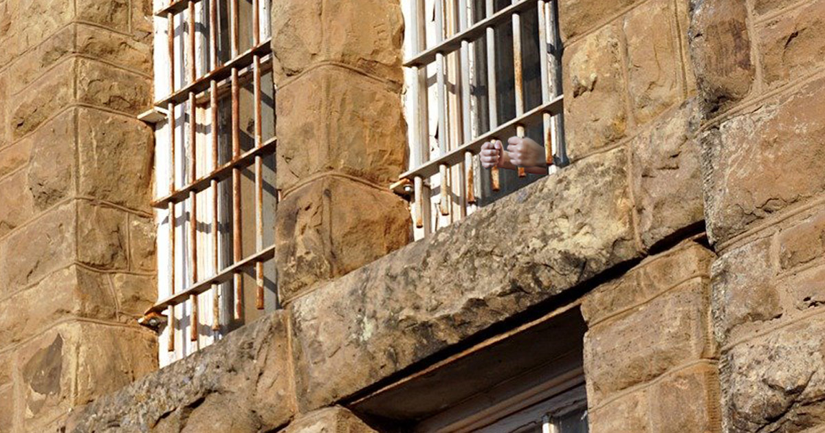 Prison with hands grasping the window bars.