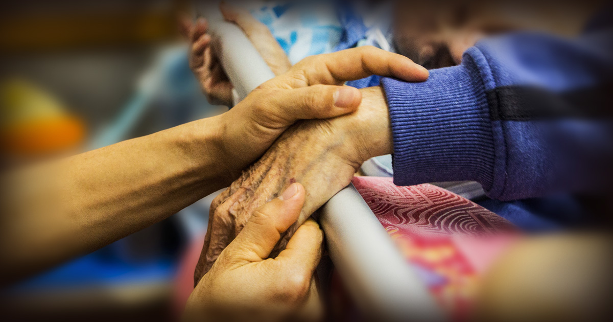 Younger hands holding an older man's hands.