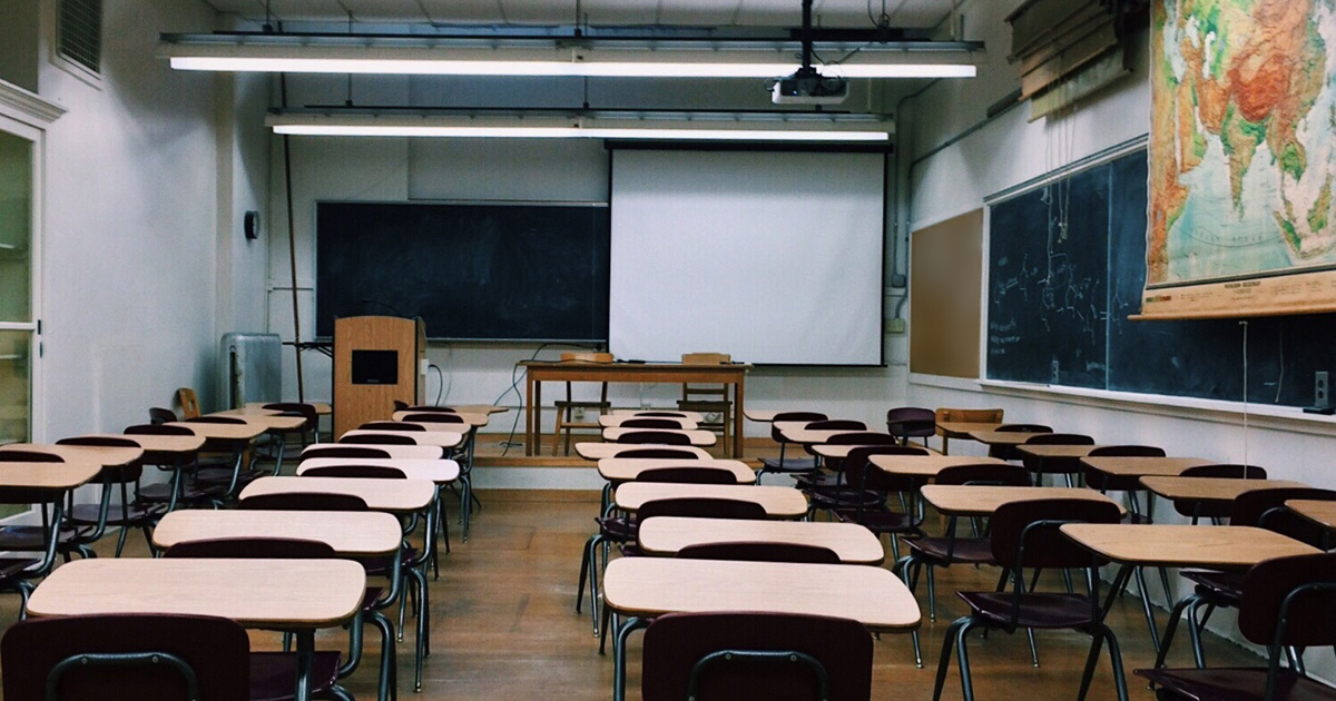 A classroom is full of empty desks, some chalkboards, and a map of Asia.