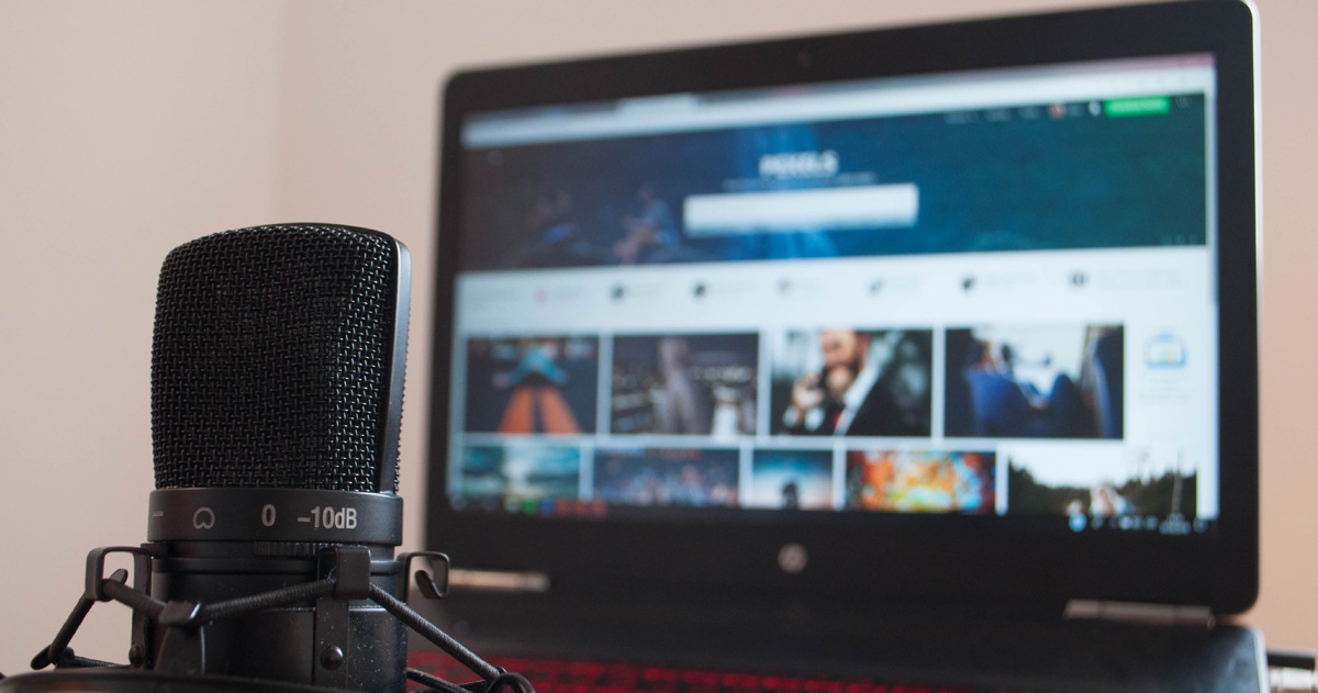 A microphone is in the foreground and an open laptop is in the background.