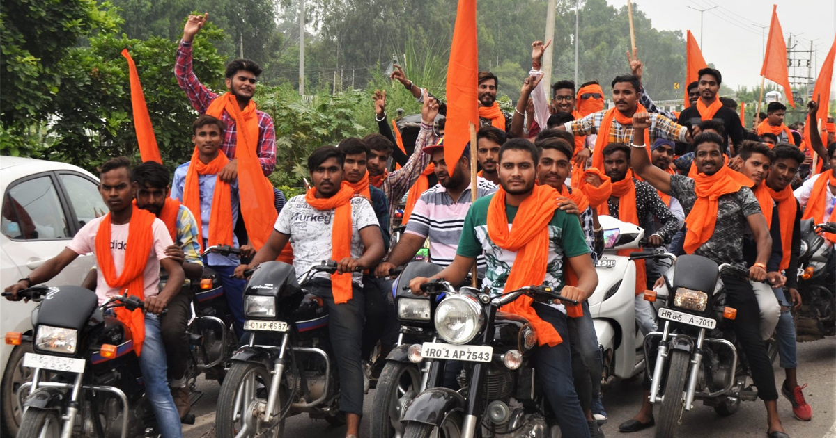 A group of people riding motorbikes, all wearing orange scarves, some carrying orange flags