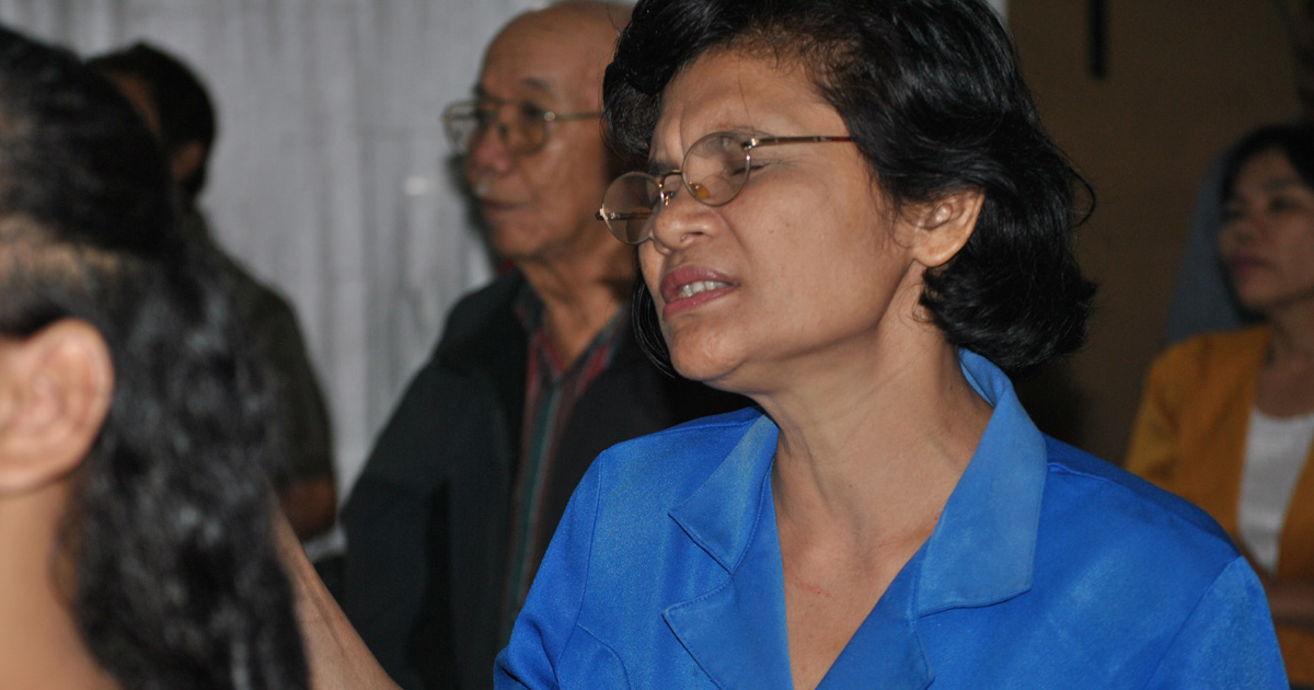 A woman is standing with her hands lifted and eyes closed. She is with a congregation.