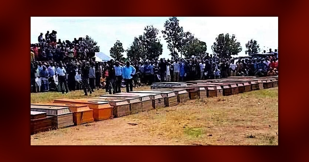 Coffins lined up with mourners gathered behind.