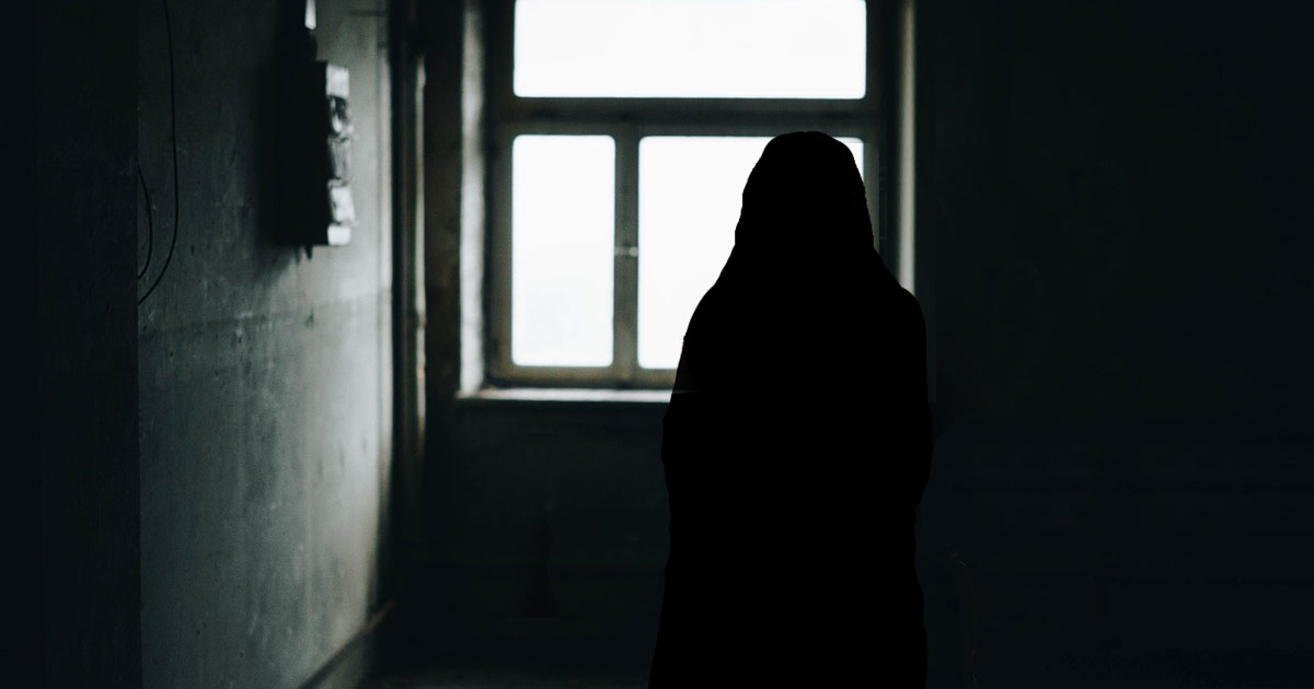 The silhouette of a young woman standing at a window.