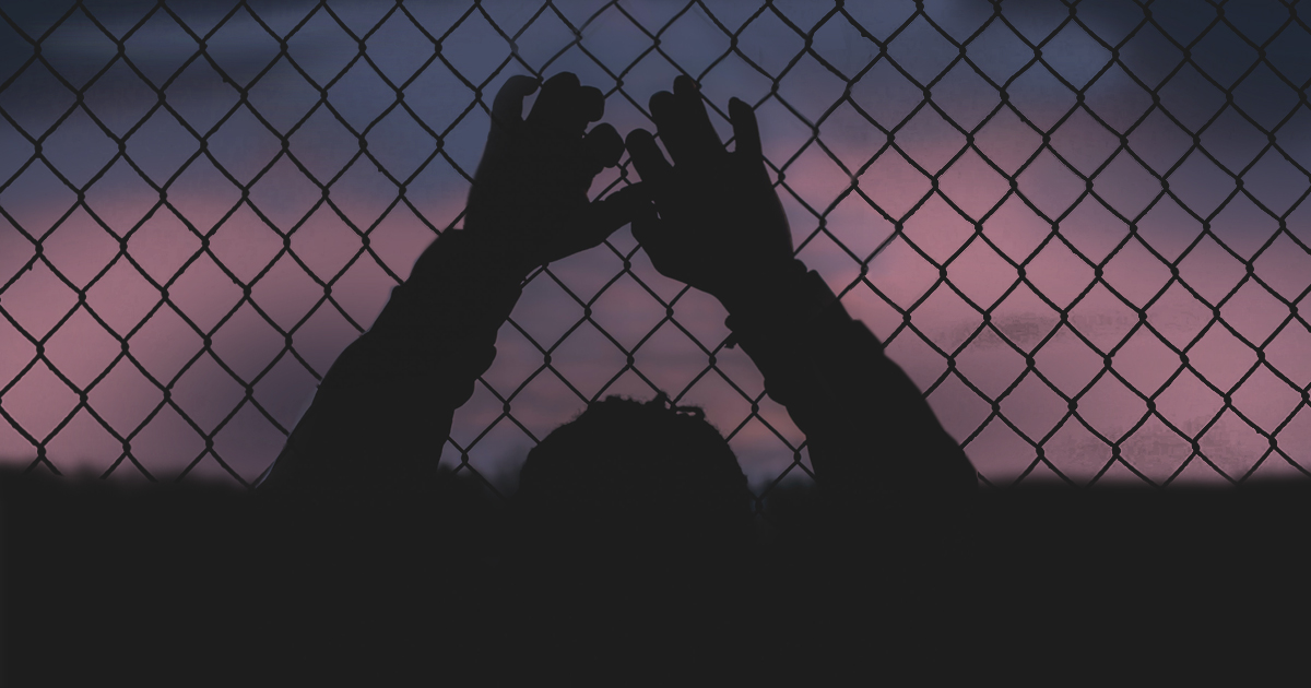 Silhouette of a man clinging to a chain link fence