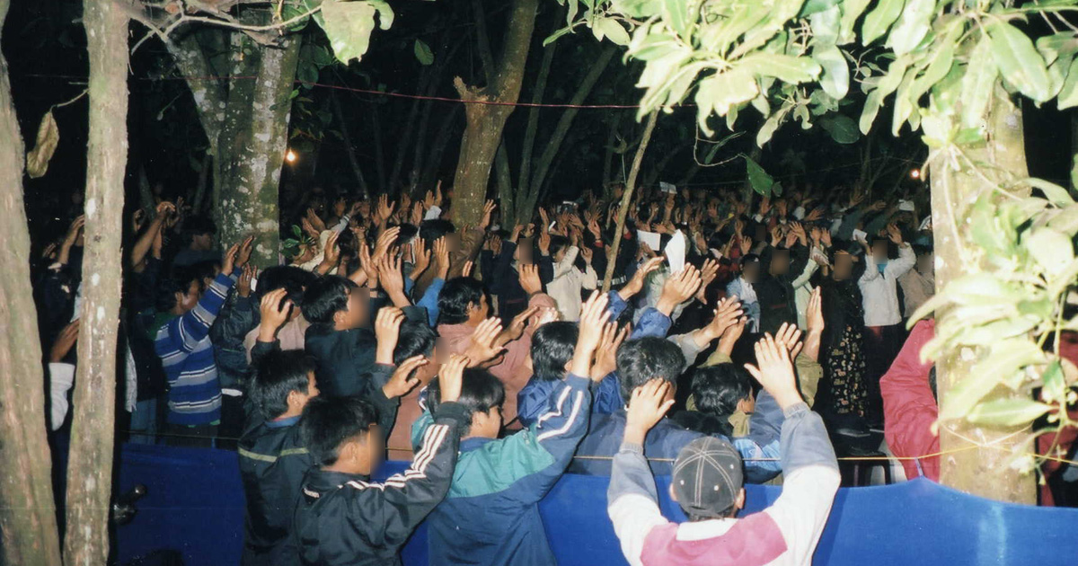 A group of believers is gathered outdoors. Most people have their hands raised.