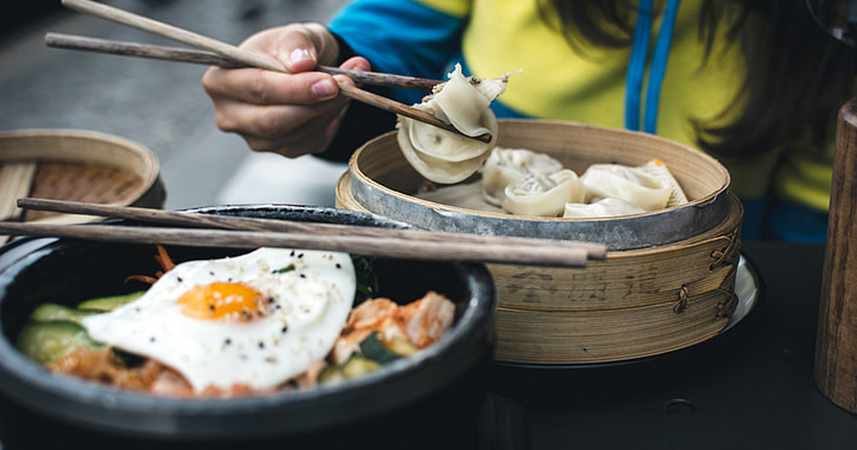 Food is placed in front of a person eating with chopsticks.