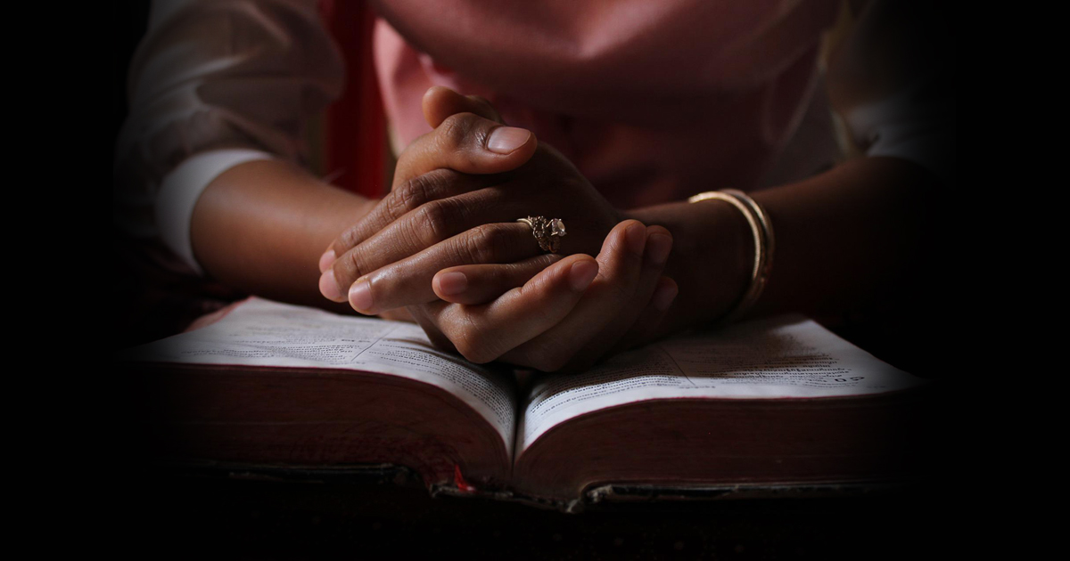 Hands clasped in prayer, resting on an open Bible