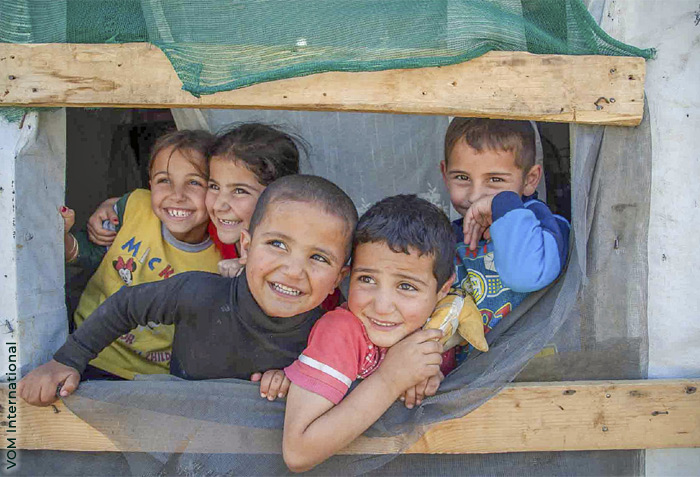 Children are smiling while looking through an opening between boards. Photo credit - VOM International